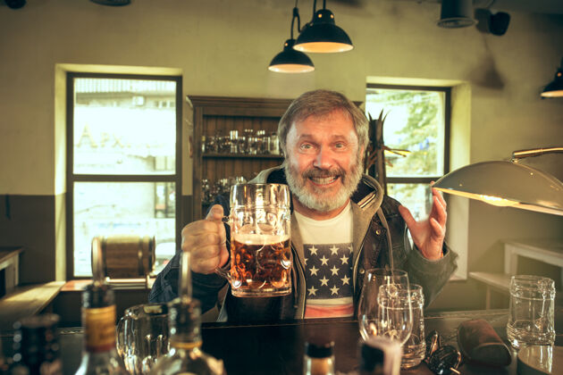 餐桌大胡子男人在酒吧喝酒 在电视上看体育节目老年人玻璃休闲