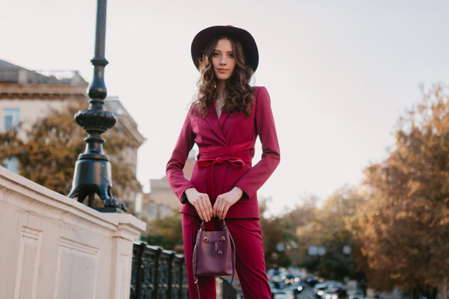 阳光穿着紫色西装的漂亮时髦女人走在城市街头 春夏秋冬时节时尚潮流戴着帽子 手拿钱包户外女人配饰