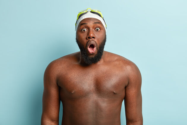 惊讶运动 娱乐和种族概念深色皮肤的男性游泳运动员看起来惊讶得屏住呼吸 额头戴着泳镜 游泳池里有赤裸的强壮身体胡须健美运动员室内