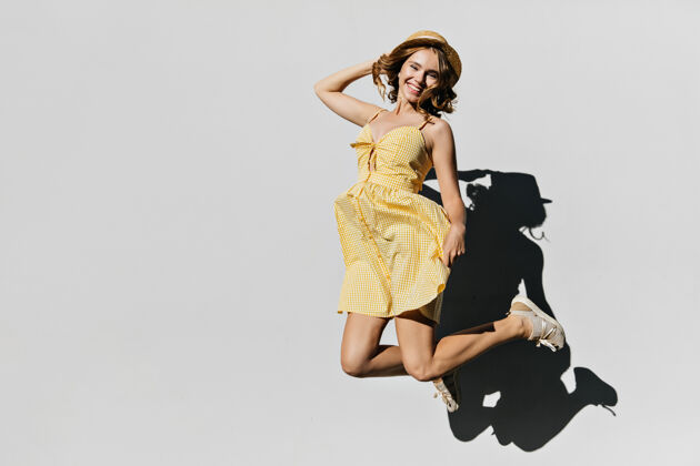 积极浅棕色的金发女人跳跃着 表达着幸福戴着帽子 穿着黄色裙子的白人女人很开心表情休息人