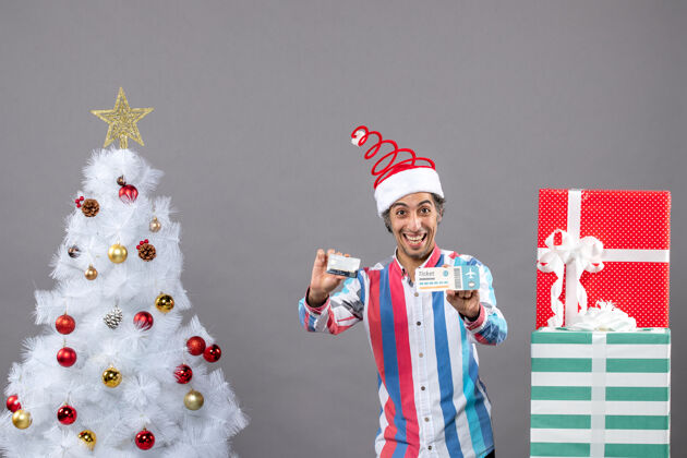 卡片正面图快乐的年轻人拿着卡片和旅行票围着圣诞树和礼物周围票快乐