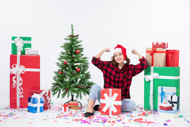 快乐年轻女子围坐在礼物和白色墙上的小圣诞树前的视图雪礼物快乐