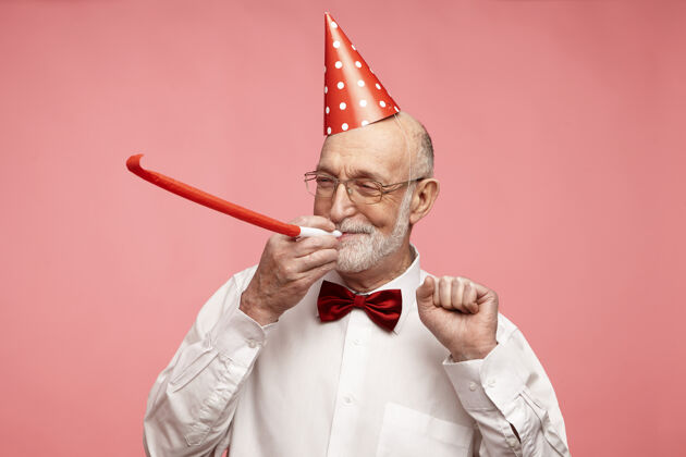 聚会一位留着浓密灰胡子的退休老人站在粉红色工作室的墙上 看上去很快乐 很漂亮礼物姿势帽子