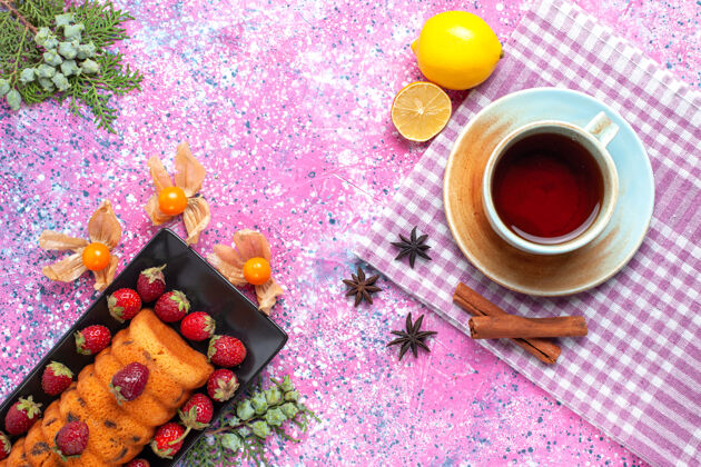 新鲜在粉红色的桌子上可以看到美味的蛋糕和新鲜的草莓 还有一杯茶水果碗甜味