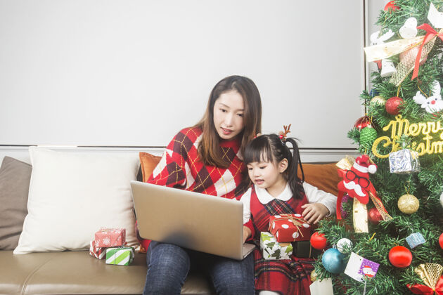 中国快乐的妈妈和小女儿在家装饰圣诞树和礼物装饰女孩圣诞节