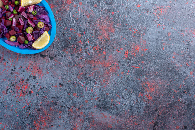 甜菜甜菜和红卷心菜沙拉放在一个盘子里 用柠檬片装饰在黑桌子上视图红色顶部视图