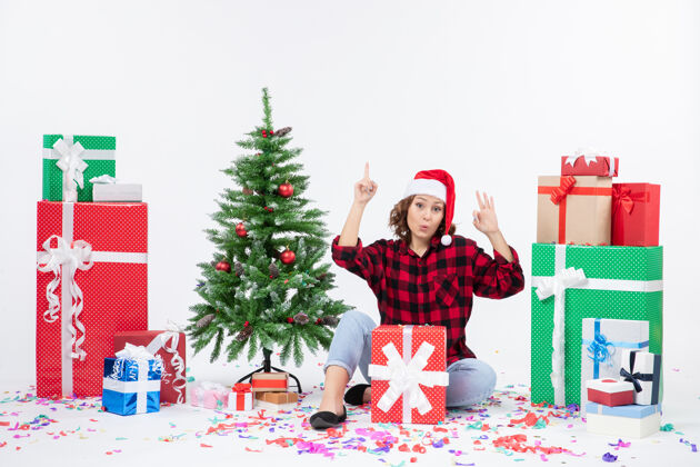 快乐年轻女子围坐在礼物和白色墙上的小圣诞树前的视图装饰人圣诞