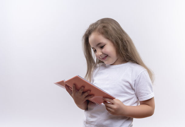 白色微笑的小女生穿着白色t恤 看着孤立的白色背景上的笔记本穿学校女孩