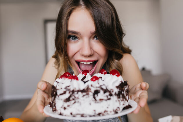微笑有趣的白人女孩摆出美味的生日蛋糕室内拍摄兴奋的女模特拿着巧克力派和浆果卡路里女士蛋糕