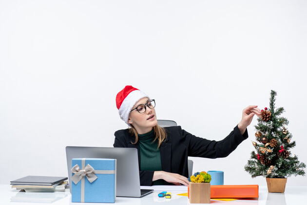 笔记本电脑新年气氛与年轻迷人的女子坐在一张桌子上 圣诞树和礼物上的圣诞老人帽子白色背景办公室圣诞老人桌子