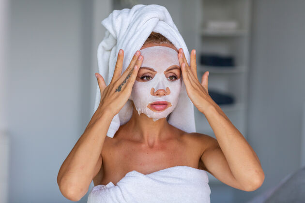 光滑冷静的白人美女肖像 头上戴着毛巾 脸上戴着化妆面具 面部皮肤护理概念女性在家里的床上放松女人肖像护理