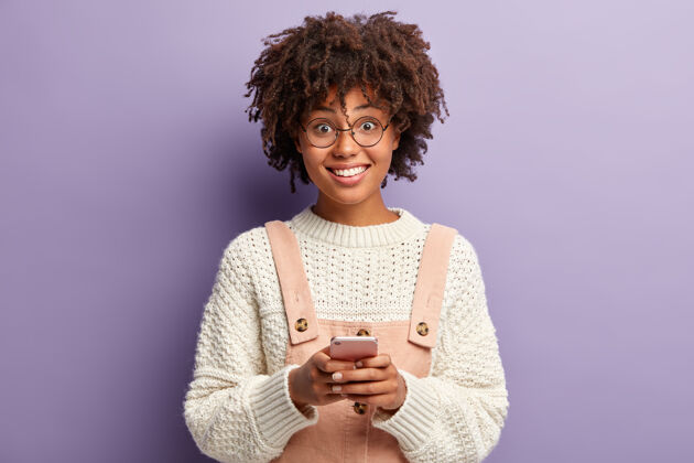 技术人与沟通的概念面带微笑的黑皮肤少女在手机上浏览社交网络 搜索搞笑视频 有愉快的表情高兴姿势聊天