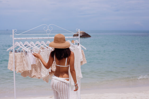度假从海滩衣架上挑选针织衣服的女人欢快时尚衣架