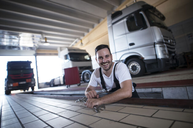 男性快乐微笑的汽车修理工在卡车修理车间拿着扳手工具工具服务汽车