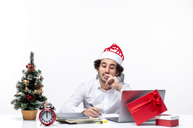 帽子忙碌的年轻商人戴着有趣的圣诞老人帽子 在白色背景的办公室里检查书写笔记和庆祝圣诞节圣诞老人写作笔记