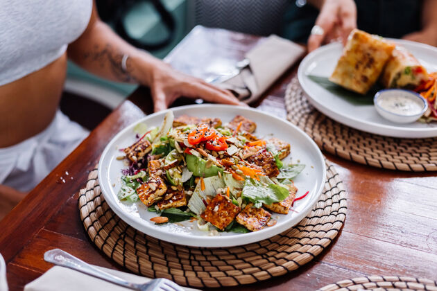 饮食在夏日咖啡厅自然采光下享用色彩缤纷的健康素食沙拉的女士营养菜肴晚餐