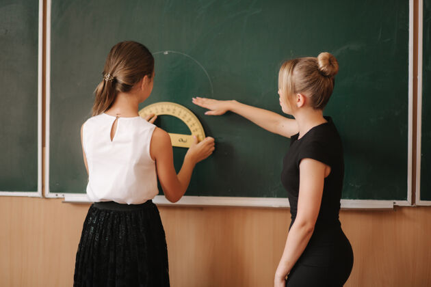 班级老师在黑板旁帮助那个女孩年轻女教师学习学校室内年轻