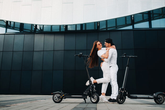 爱一个女孩和一个男孩骑着电动滑板车在城市里走来走去 一对恋人骑着滑板车夫妻关系踢摩托车