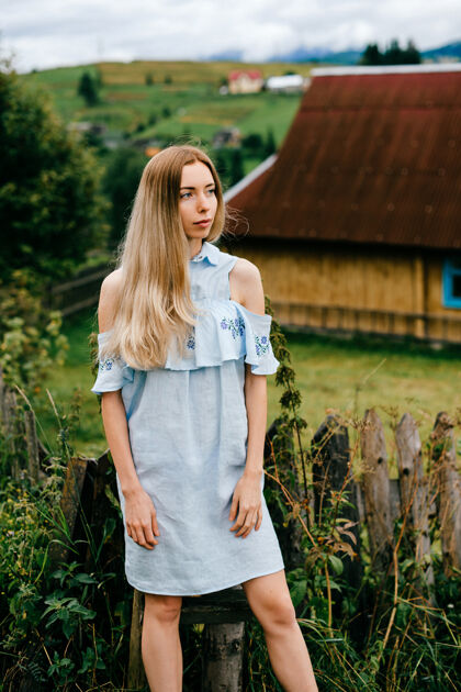 金发年轻漂亮的金发碧眼的女孩 穿着蓝色的裙子 在乡下的乡间小屋上摆姿势年轻自然优雅