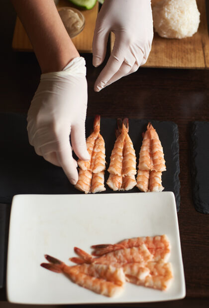 手在餐厅里 一个戴着手套的女人正在为卷寿司准备虾烹饪亚洲过程