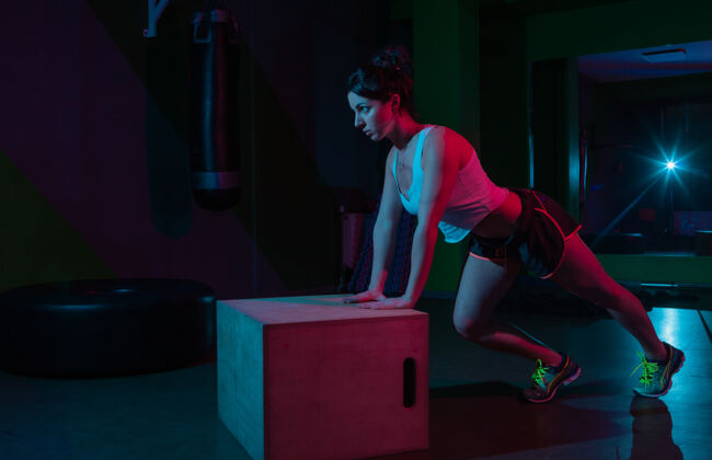 肌肉年轻健康的女性俯卧撑从一个霓虹灯梯度红蓝色的暗墙上功能训练概念木盒子活力身体训练