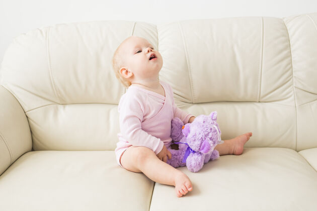客厅童年 婴儿期和人的概念-快乐的小女婴坐在家里的沙发上生活快乐小