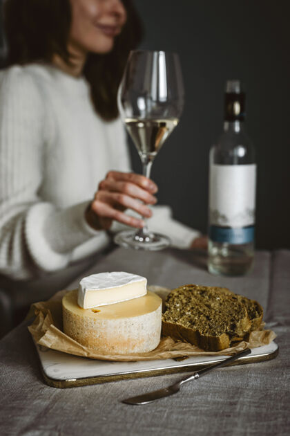 年轻一个女人拿着一杯白葡萄酒 一瓶酒 几种奶酪和面包放在砧板上垂直生活方式照片场景瓶子布里