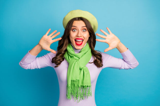 黑发照片中时髦的旅行家女士举手张开嘴兴奋的心情尖叫着戴上绿色贝雷帽紫色高领围巾孤立的亮蓝色墙壁女人冬天有趣