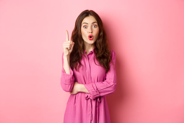 惊人年轻时尚的女性女孩说着建议 有了解决办法 有了主意 在尤里卡牌上竖起手指 站在粉红色的墙上手势乐观成人