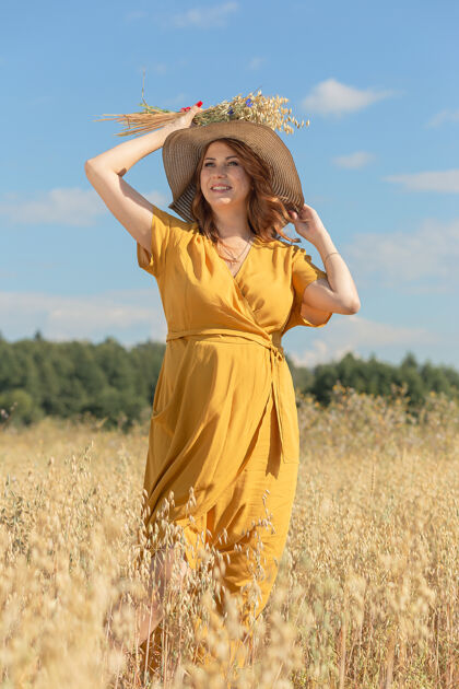人在一个阳光明媚的夏日 一位年轻漂亮的孕妇穿着黄色的裙子 戴着黄色的帽子 走过一片麦田肚子天空自然