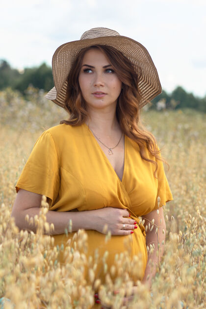 太阳在一个阳光明媚的夏日 一位年轻漂亮的孕妇穿着黄色的裙子 戴着黄色的帽子 走过一片麦田温暖婴儿麦田