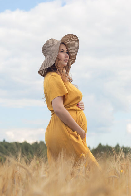肥料在一个阳光明媚的夏日 一位年轻漂亮的孕妇穿着黄色的裙子 戴着黄色的帽子 走过一片麦田肚子黄色生命