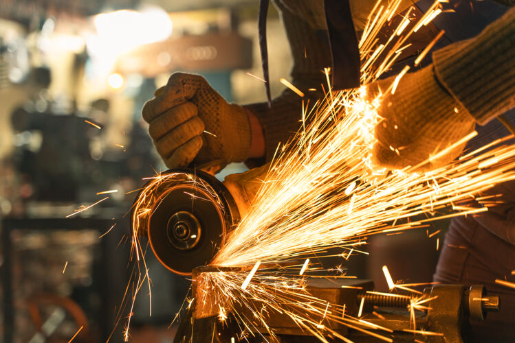 工业穿着特殊衣服和护目镜的锁匠在工厂工作生产.金属用角磨机加工手工车轮火花