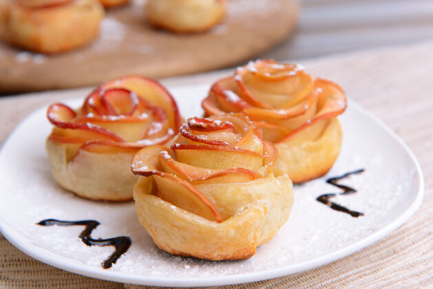 巧克力美味的松糕与苹果形状的玫瑰在盘子上桌上特写形状花瓣饼干