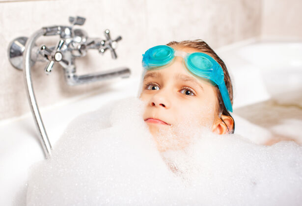 鼻子有趣的积极的白人小女孩戴着泳镜在洗澡欢呼肥皂美容