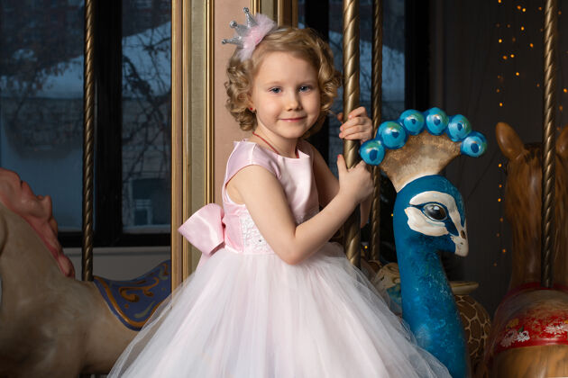 近一个穿着粉色裙子戴着皇冠的小女孩和一只白兔坐在旋转木马上节日公主新的