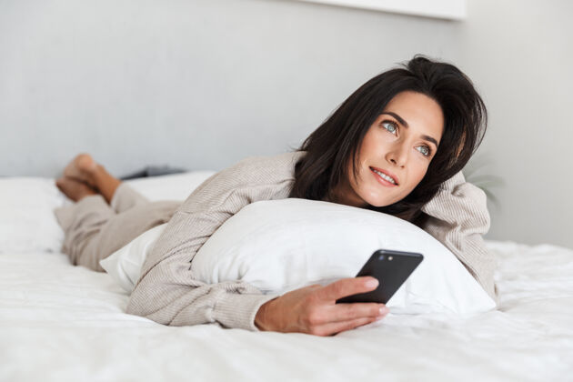 可爱一张30多岁的欧洲女人在明亮的房间里躺在床上用手机的照片谎言小玩意手机