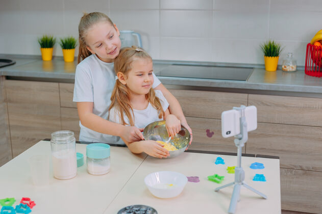 女儿两位姐妹博客作者在厨房做饭 并用智能手机拍摄烹饪视频父母厨房孩子