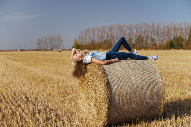 玻璃一位年轻漂亮的女村民 穿着牛仔裤 站在地里的一捆干草上稻草干草牛仔裤