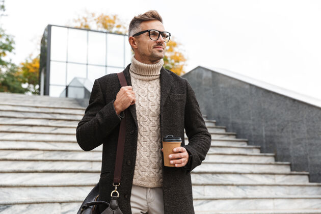 帅气30多岁的成熟男人戴着眼镜 穿过城市街道 拿着外卖咖啡夹克城镇外卖