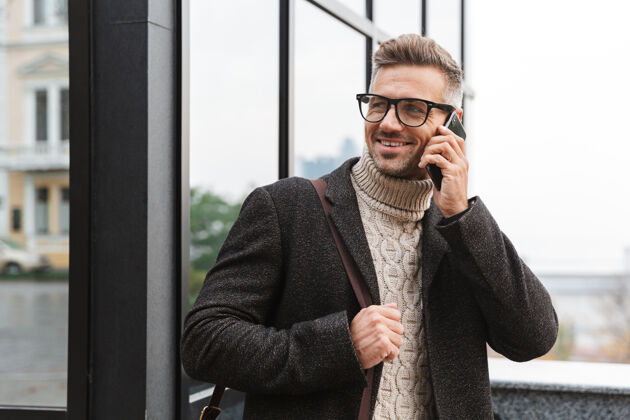 成人30多岁的留胡子男人戴着眼镜 穿过城市街道 使用智能手机站立漫步白种人