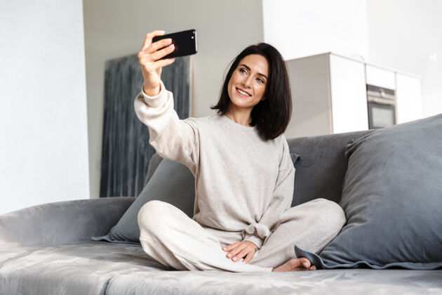 设备一张30多岁的微笑女子坐在明亮公寓的沙发上用手机自拍的照片室内沙发自拍