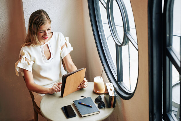 化妆品坐在咖啡桌旁 微笑的金发女郎正在使用平板电脑上的应用程序互联网年轻人欢呼