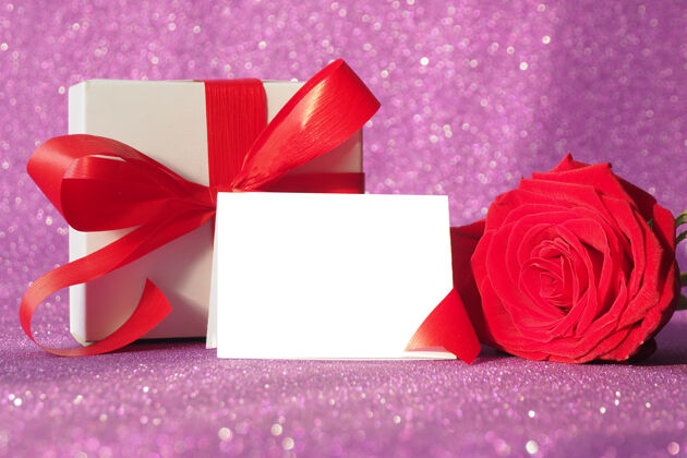 花礼盒上有一个红色的蝴蝶结和一朵红色的玫瑰 背景是紫色的闪闪发光浪漫花束花瓣