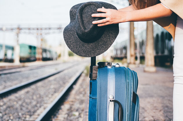 铁路在火车站把帽子放在手提箱上的女人旅行者行李独自