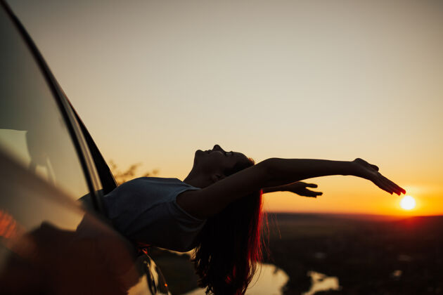 剪影在夏日夕阳下欣赏美丽景色的女人 在夕阳下举手坐在车里风景户外年轻