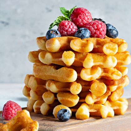 荷兰早餐用新鲜酥脆的比利时华夫饼 配上成熟的浆果（覆盆子 蓝莓 黑莓） 薄荷和糖粉放在木板上 背景清淡早上美味华夫饼