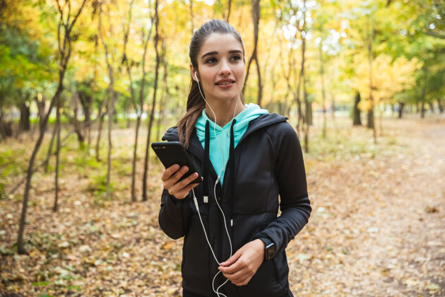 成人照片中 一位年轻漂亮的健身女士在公园里用手机和耳机听音乐活力女人运动员