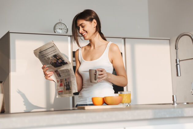 马克杯微笑的年轻女孩早上站在厨房 看报纸 喝茶周末放松享受