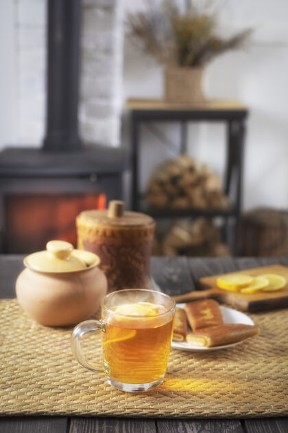 食物馅饼茶在燃烧的壁炉背景下 蜂蜜和柠檬放在木桌上村庄气氛早餐
